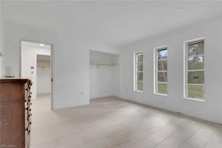 Spacious room featuring light-toned tile flooring, three large windows, a generous closet with shelving, and an additional doorway opening to another space