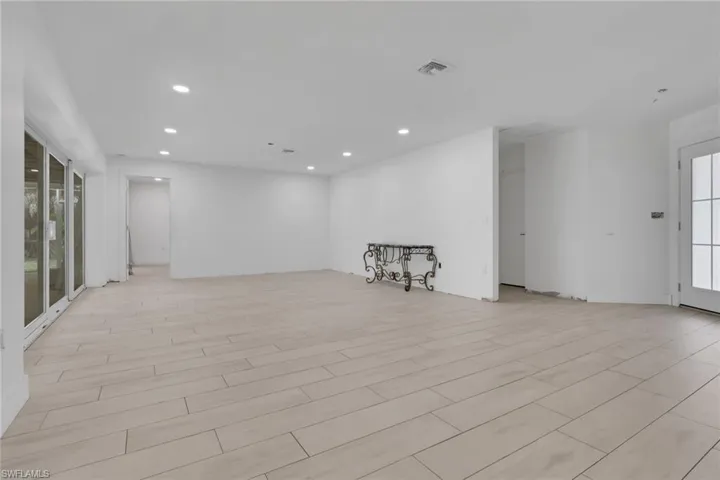 Spacious room featuring light-toned plank flooring, white walls, recessed ceiling lighting, and expansive glass panel doors opening to the exterior