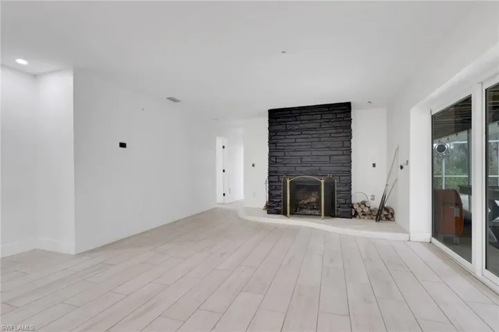 Spacious room featuring light wood-finish flooring, a prominent black stone-clad fireplace, and recessed ceiling lighting