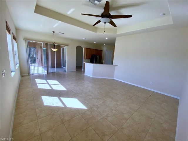 Empty room featuring a tray ceiling, arched walkways, and ceiling fan