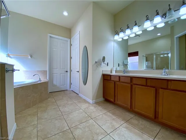 Full bath with double vanity, a garden tub, light tile patterned floors, and a shower stall
