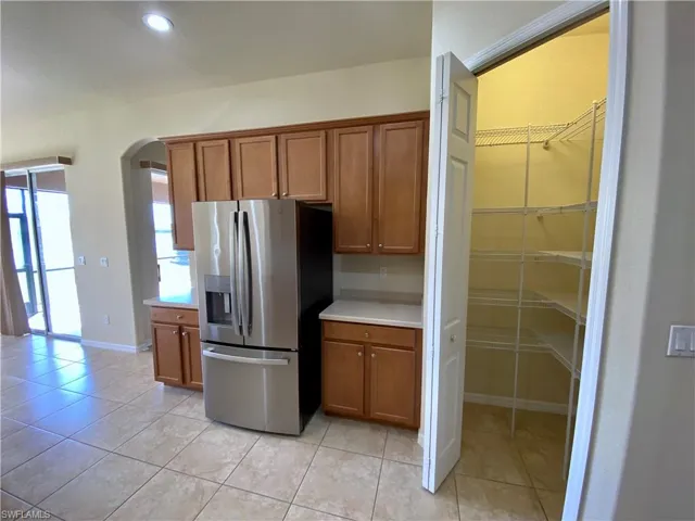 Kitchen featuring brown cabinetry, stainless steel refrigerator with ice dispenser, arched walkways, light countertops, and recessed lighting