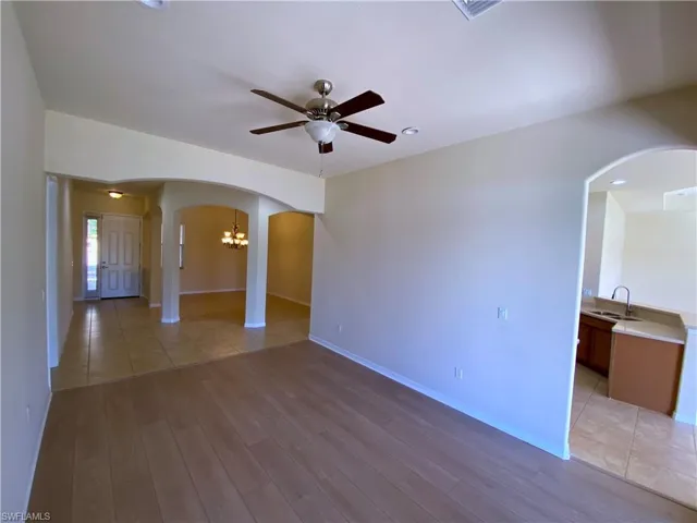 Spare room featuring arched walkways, a ceiling fan, light wood-style flooring, and a chandelier