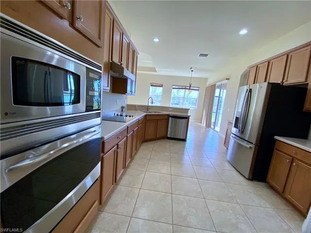 Kitchen with brown cabinetry, a peninsula, appliances with stainless steel finishes, decorative light fixtures, and recessed lighting