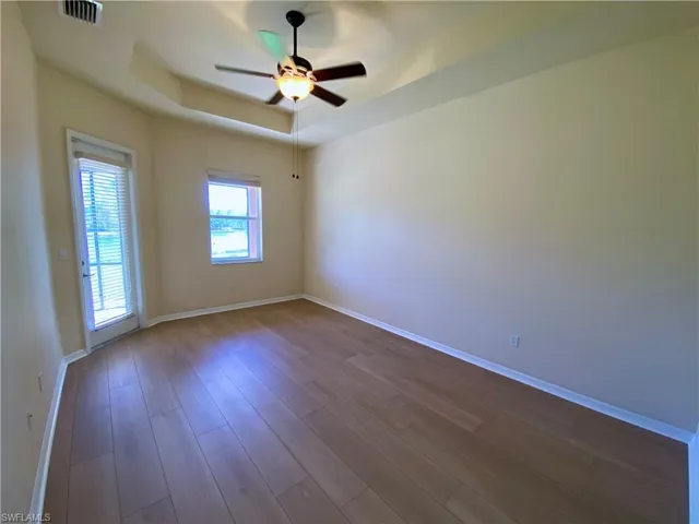 Empty room featuring a raised ceiling, wood finished floors, and a ceiling fan