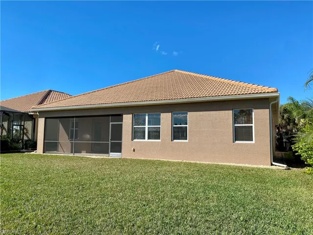 Rear view of house with a yard, stucco siding, a tiled roof, and a sunroom