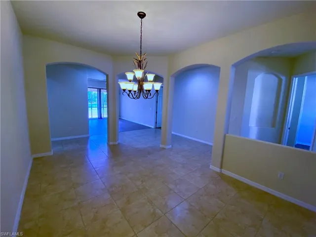 Empty room with arched walkways, a chandelier, and light tile patterned floors