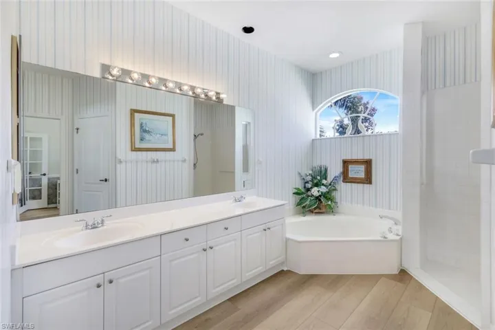 Bathroom with wallpapered walls, a walk in shower, a garden tub, double vanity, and wood finished floors
