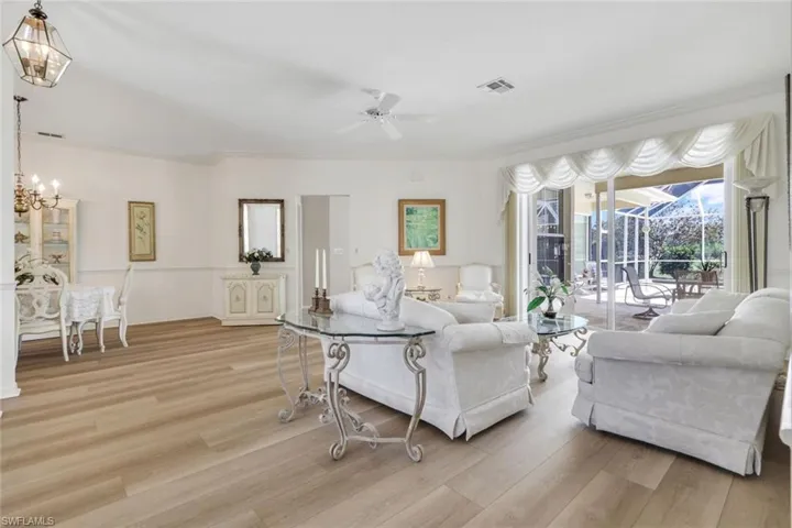 Living room featuring a ceiling fan, light wood-type flooring, a chandelier, and ornamental molding