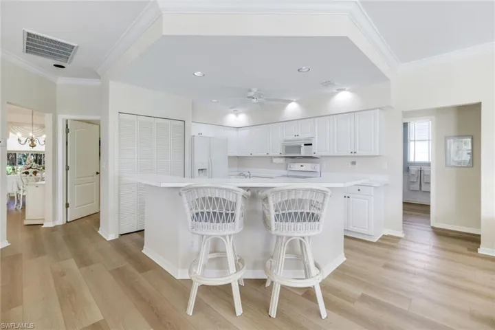 Kitchen featuring white appliances, light countertops, a kitchen breakfast bar, white cabinetry, and crown molding