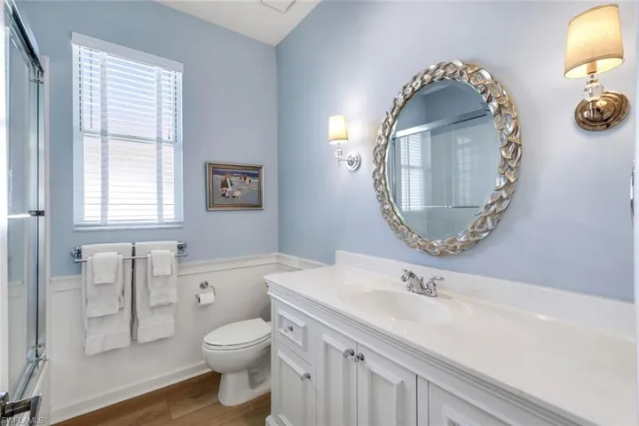 Full bathroom with wood finished floors, plenty of natural light, toilet, vanity, and a wainscoted wall