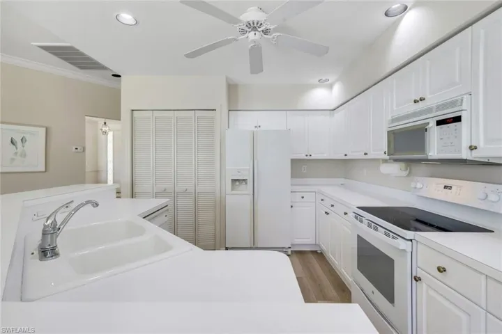 Kitchen featuring white appliances, a sink, white cabinets, light wood finished floors, and ornamental molding