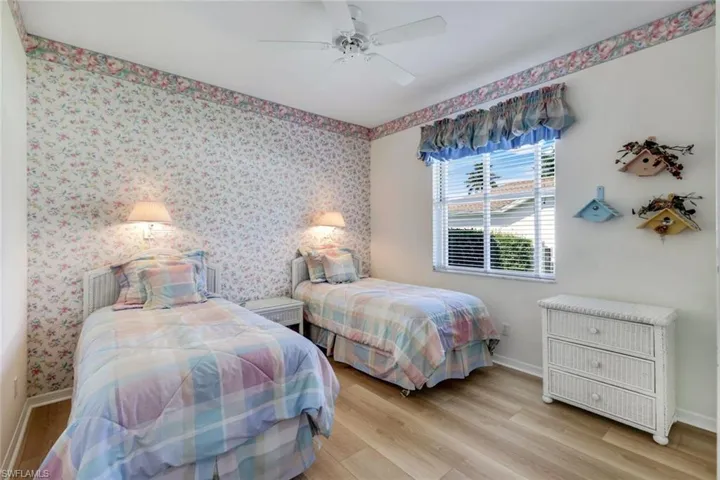 Bedroom with wallpapered walls, baseboards, wood finished floors, and ceiling fan