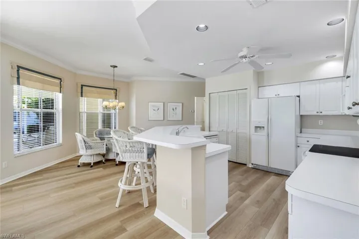 Kitchen featuring white fridge with ice dispenser, crown molding, light countertops, ceiling fan, and white cabinetry
