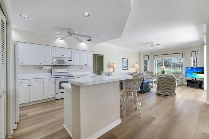 Kitchen featuring white appliances, ceiling fan, open floor plan, light countertops, and white cabinetry