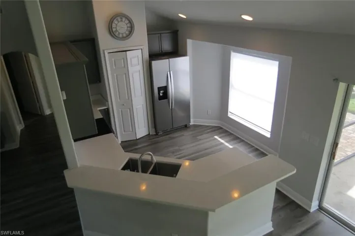 Kitchen featuring dark wood-type flooring, stainless steel refrigerator with ice dispenser, a healthy amount of sunlight, and lofted ceiling