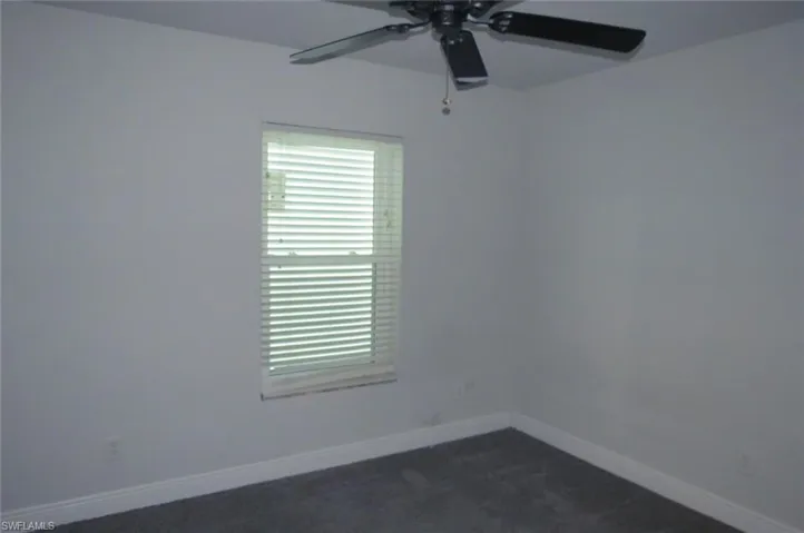Empty room featuring dark colored carpet and ceiling fan