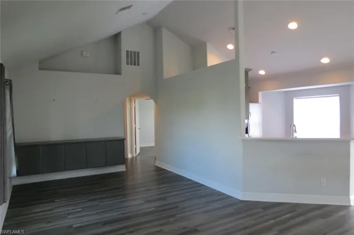 Empty room with high vaulted ceiling and dark wood-type flooring