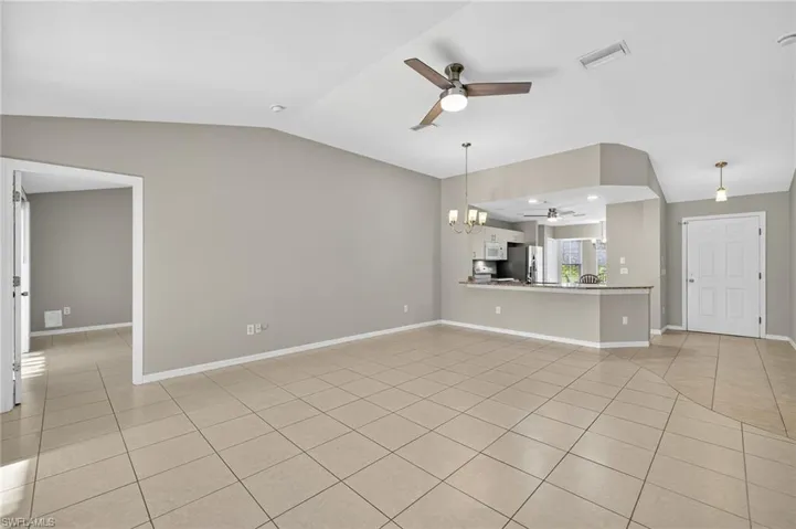 Unfurnished living room featuring a chandelier, light tile patterned floors, lofted ceiling, and a ceiling fan