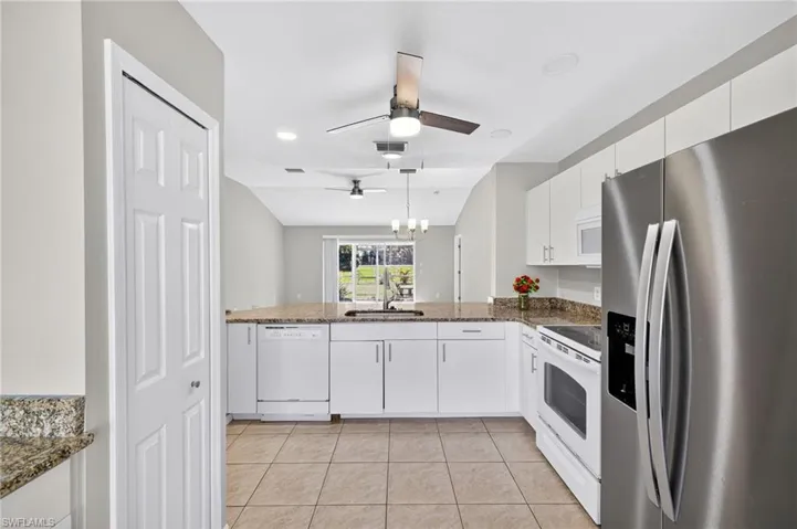 Kitchen with white appliances, white cabinetry, light tile patterned floors, and dark stone countertops