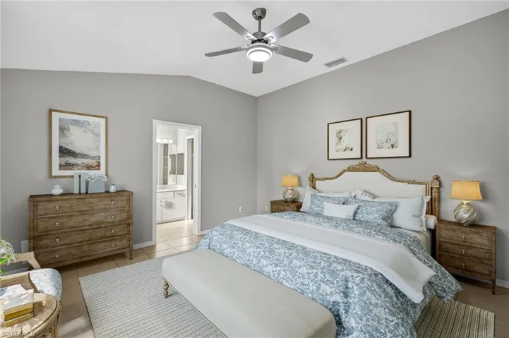 Bedroom featuring lofted ceiling, ceiling fan, light tile patterned floors, and ensuite bath