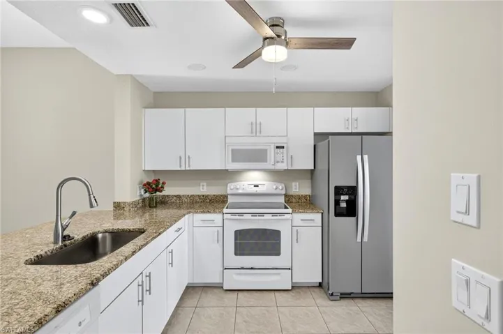 Kitchen with white appliances, white cabinets, dark stone counters, and recessed lighting