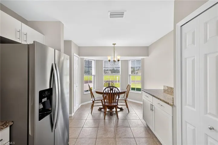 Kitchen with white cabinetry, stainless steel refrigerator with ice dispenser, dark stone counters, hanging light fixtures, and light tile patterned floors