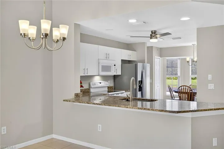 Kitchen featuring a chandelier, decorative light fixtures, a peninsula, white appliances, and dark stone counters