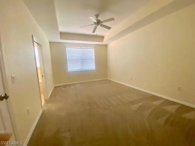Unfurnished room with a raised ceiling, carpet flooring, and ceiling fan