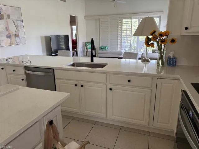 Kitchen with stainless steel appliances, sink, ceiling fan, light tile patterned floors, and white cabinets