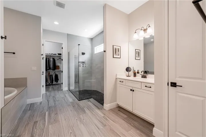 Bathroom with a spacious closet, vanity, a tile shower, a bath, and light wood finished floors