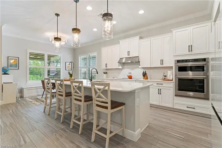 Kitchen with a breakfast bar, ornamental molding, pendant lighting, white cabinetry, and double oven