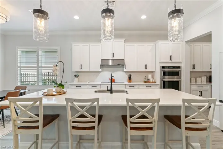 Kitchen featuring white cabinetry, a spacious island, crown molding, hanging light fixtures, and a breakfast bar