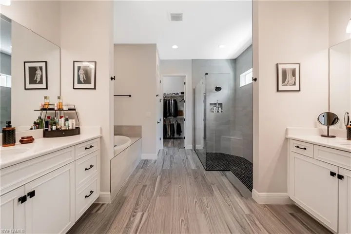 Full bathroom featuring a shower stall, a walk in closet, two vanities, a garden tub, and light wood finished floors