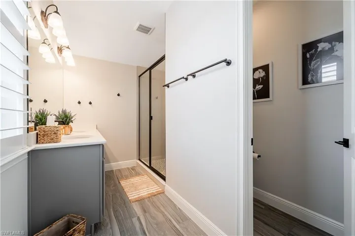 Full bath with double vanity, a shower stall, dark wood finished floors, and healthy amount of natural light