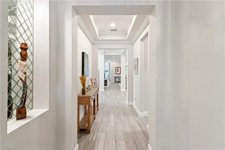 Hall with a tray ceiling, light wood-style floors, crown molding, and recessed lighting