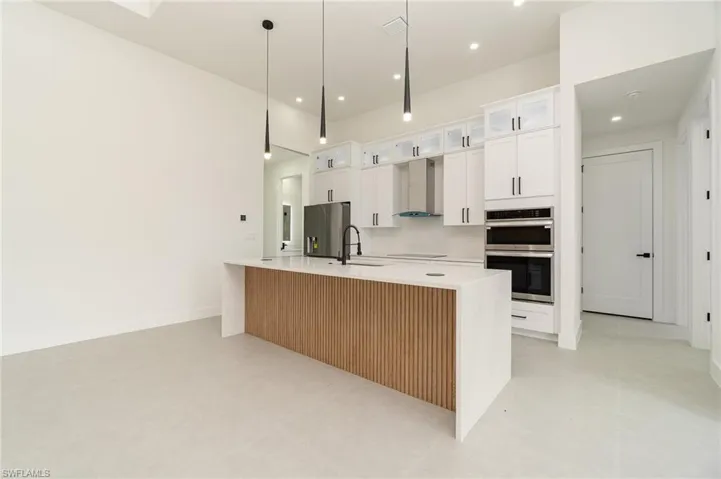 Kitchen with stainless steel appliances, sink, white cabinetry, wall chimney exhaust hood, and a large island with sink