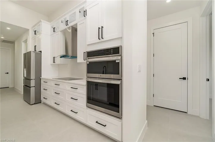Kitchen with appliances with stainless steel finishes, white cabinetry, light tile patterned floors, and wall chimney exhaust hood