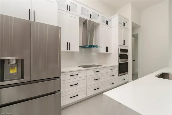 Kitchen with light tile patterned flooring, white cabinets, wall chimney exhaust hood, light stone counters, and appliances with stainless steel finishes