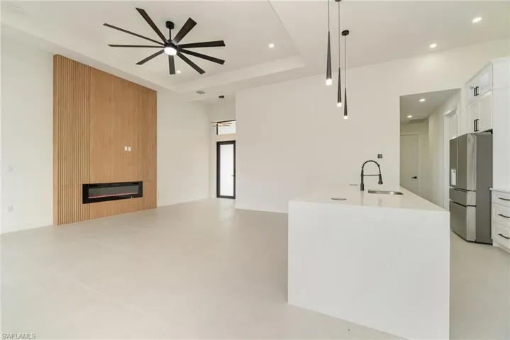Kitchen with a large fireplace, decorative light fixtures, a tray ceiling, white cabinets, and stainless steel fridge