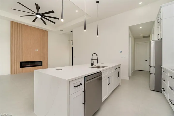 Kitchen featuring appliances with stainless steel finishes, ceiling fan, a large fireplace, white cabinetry, and a tray ceiling
