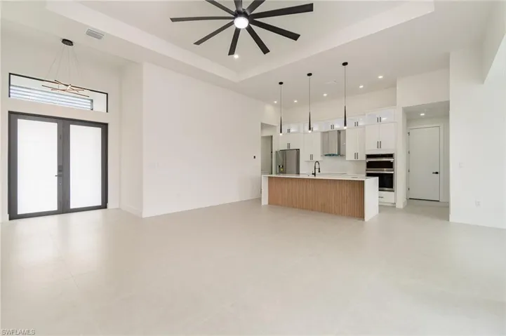 Unfurnished living room featuring ceiling fan, sink, french doors, a raised ceiling, and light tile patterned floors