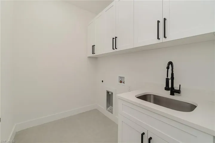 Clothes washing area featuring sink, cabinets, light tile patterned floors, hookup for an electric dryer, and washer hookup