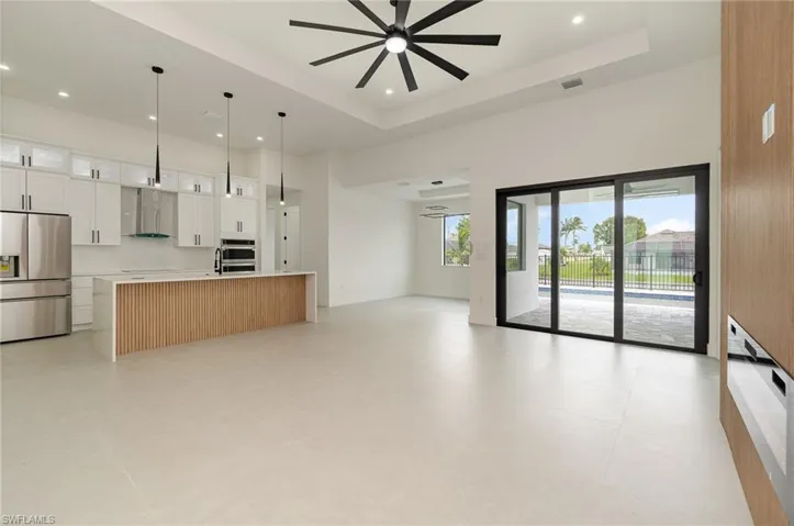 Kitchen with light tile patterned floors, a raised ceiling, a center island with sink, and stainless steel refrigerator with ice dispenser