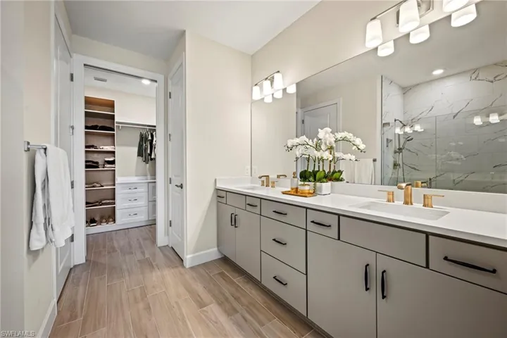 Bathroom featuring double vanity, a marble finish shower, wood finish floors, and a walk in closet