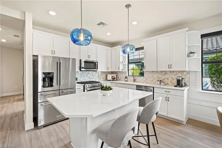 Kitchen with high end appliances, a kitchen island, white cabinets, and decorative light fixtures