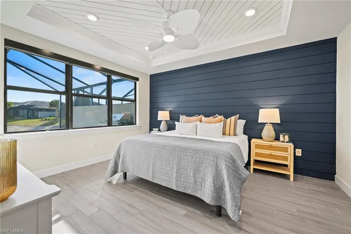 Bedroom with wood walls, an accent wall, wood finish floors, a tray ceiling, and a ceiling fan