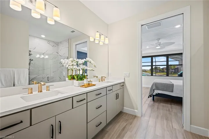Full bath with a marble finish shower, double vanity, connected bathroom, and wood finish floors