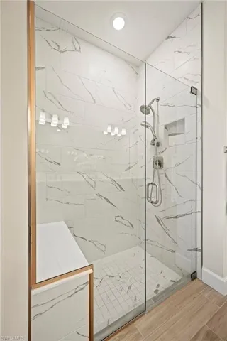 Bathroom with a marble finish shower, wood finished floors, and recessed lighting