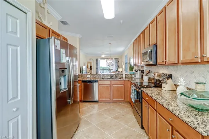 Kitchen featuring appliances with stainless steel finishes, light tile patterned floors, decorative backsplash, a peninsula, and crown molding